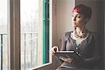 Young woman sitting by window, using digital tablet