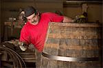 Male cooper using hammer in cooperage with whisky casks