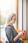 Young woman, wearing headphones, sitting in cafe, holding smartphone