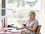 Mature businesswoman reading text message on smartphone at home desk