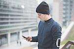 Young male runner reading smartphone text on footbridge