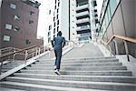 Rear view of young male runner running up city stairs
