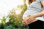 Pregnant woman holding belly, outdoors, mid section