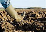 Close up of farmers rubber boot walking on ploughed field