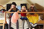 Three sisters, sitting on bed,  wearing fancy dress costumes, covering mouth, ears and eyes