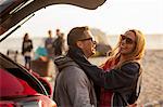 Couple relaxing behind vehicle on beach