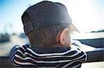 Rear view of boy with cap leaning against railing