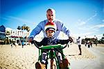 Father guiding son on bicycle at beach, Brooklyn, New York, USA
