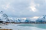 Distant view of waterfront village and snow capped mountains, Reine, Lofoten, Norway