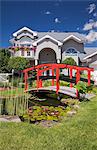 Grey brick cottage style residential home and landscaped  manicured garden with red wooden footbridge, Quebec, Canada