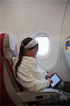 Young girl sitting in seat on aeroplane using digital tablet