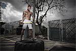 Poised male boxer standing on truck tyre holding sledge hammer in yard