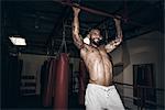 Male boxer doing pull ups with gritted teeth in gym