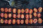 Overhead view of rows of halved roasted tomatoes on baking tin