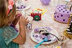 Side view of of girl sitting at birthday party table eating purple cake