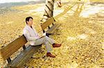 Senior Japanese man sitting on a bench with a book in a city park in Autumn