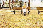 Senior Japanese woman sitting on a bench with a book in a city park in Autumn