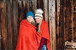 Two young female friends wrapped in red blanket outside wooden cabin