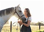 Portrait of teenage girl and her grey horse in sunlit field