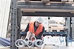 Young male warehouse worker selecting industrial pipe from shelf