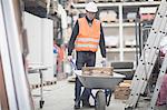 Young male warehouse worker pushing wheelbarrow in warehouse