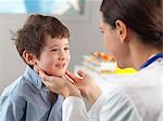 Doctor checking glands of young boy in clinic