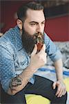 Young bearded man smoking pipe on bed