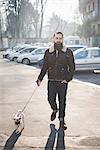 Young bearded man walking dog on street