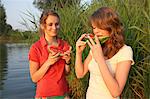 Two young women eating watermelon slices at lakeside