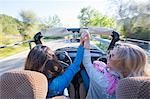 Two mature women, holding hands, in convertible car, rear view