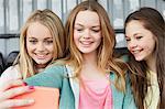 Three girls posing for smartphone selfie in shelter