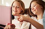 Two girls on sofa laughing and pointing at digital tablet