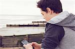 Teenage boy at seaside texting on smartphone, Southend on Sea, Essex, UK