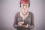 Studio portrait of young woman with short pink hair choosing music on smartphone