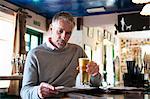 Mature man drinking beer and reading newspaper in pub