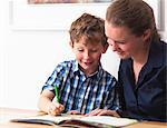 A six year old being helped with his homework by his mother at home