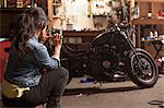 Female mechanic in workshop, taking photograph of motorcycle using smartphone