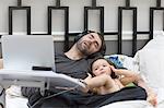 Female toddler listening to headphone music in bed whilst father sleeps