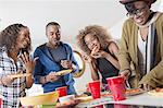 Four adult friends chatting and eating party food in kitchen