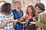 Four adult friends  laughing and eating party food in kitchen