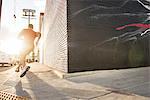 Rear view of male runner running on sidewalk