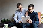 Father and teenage son reading digital tablet on sofa