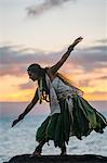 Woman hula dancing on coastal rocks wearing traditional costume at sunset, Maui, Hawaii, USA
