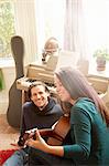 Young couple playing acoustic guitar in living room