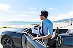 Young businessman getting out of car at coastal parking lot with paperwork