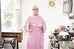 Senior woman standing in kitchen holding plate of food