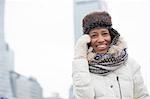 Cheerful woman in winter wear using cell phone outdoors