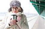 Portrait of smiling woman in warm clothing holding insulated drink container