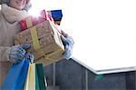 Midsection of woman with stacked gifts and shopping standing by window during winter