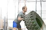 Side view of dedicated man flipping tire in crossfit gym